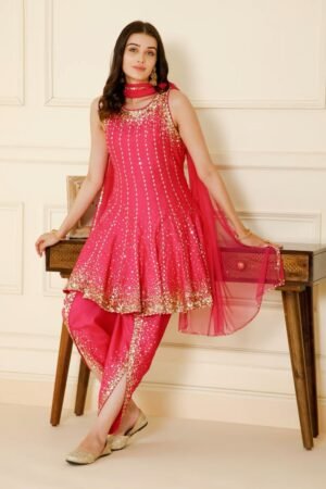 a vibrant fuchsia pink Patiyala suit. The sleeveless, flared kurti is adorned with vertical lines of gold sequins and embroidery, and features a thick, embellished gold border at the hem. She is wearing matching dhoti-style pants with gold detailing and a sheer pink dupatta.