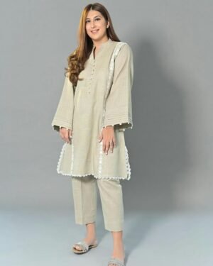 light beige linen kurti and pants set. The short, straight kurti is decorated with intricate white floral embroidery and scalloped lace trim along the hem and the cuffs of the flared sleeves. She is wearing matching straight-fit linen pants